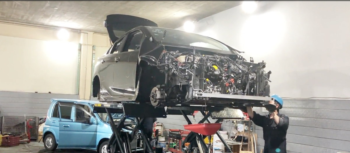 リフト上の車を1台ずつていねいに解体し、使える部品を取り外して中古パーツとして活かす作業風景（株式会社ヤツヅカ）